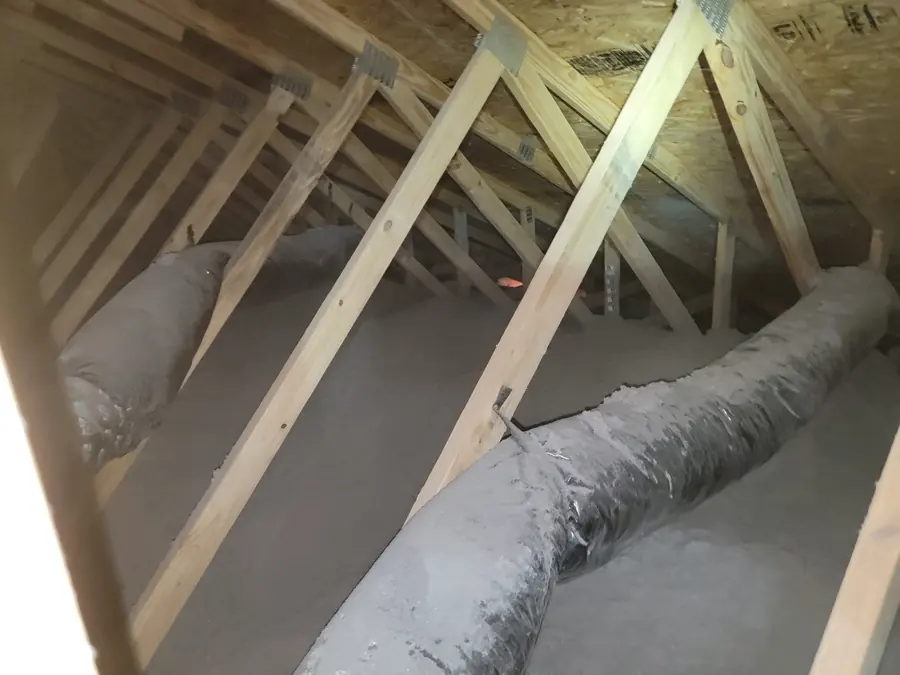 New wood-truss attic with gray blown-in cellulose insulation covering the floor and flexible ducts running through it