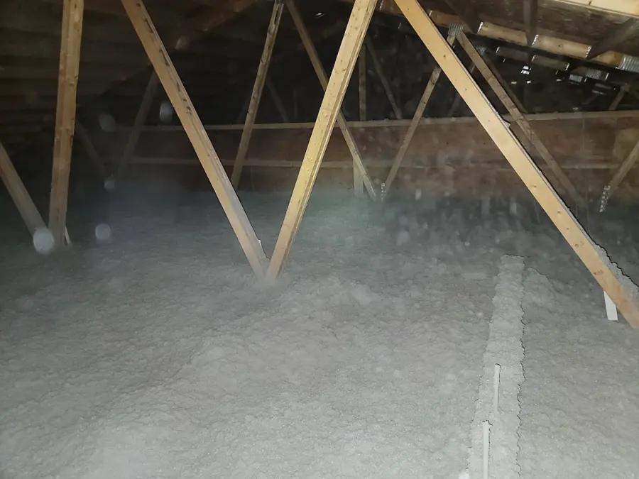 Attic floor covered in deep gray blown-in cellulose insulation between W-shaped wood roof trusses