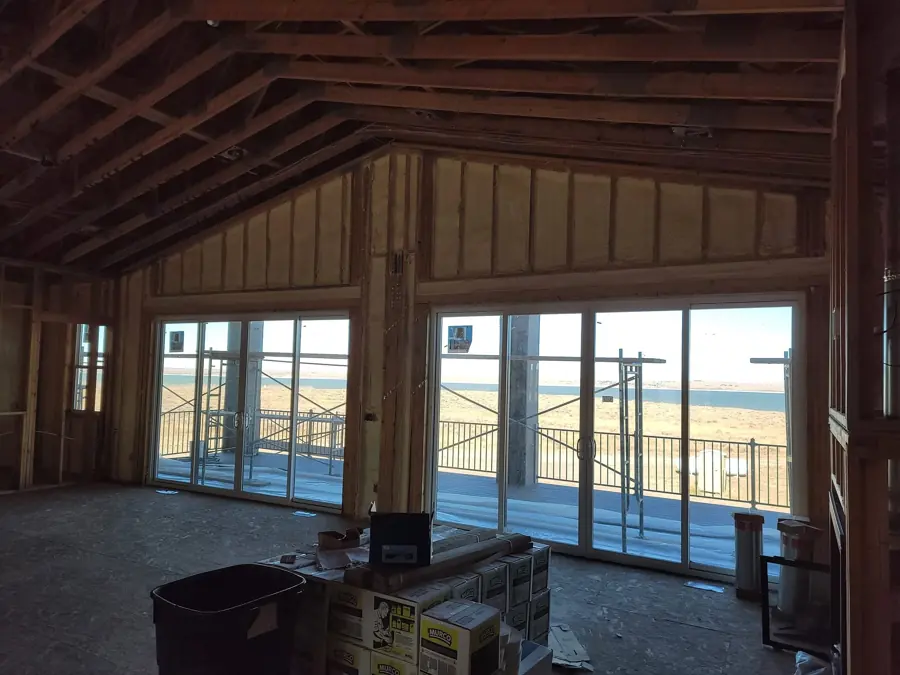 Framed new home with spray foam in the gable wall stud bays above large sliding glass doors and a view of open land