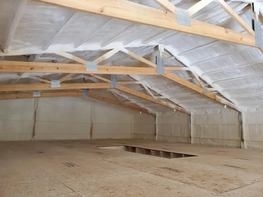 White closed-cell spray foam on roof underside and walls above an OSB loft floor with a floor access opening