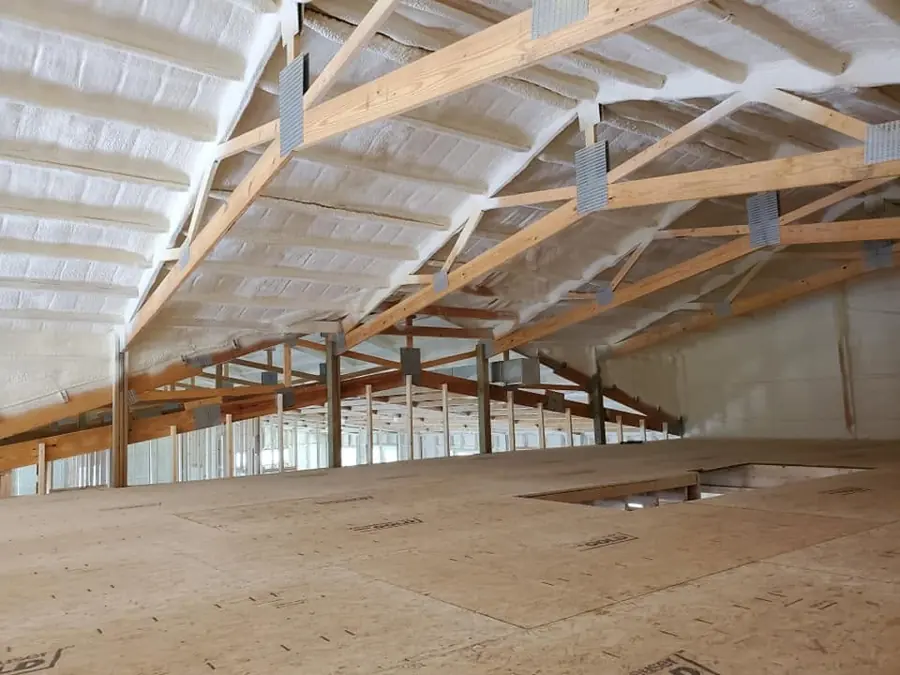 White closed-cell spray foam on the underside of a roof between wood trusses above an OSB-floored loft