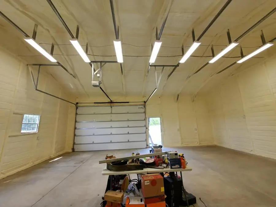 Garage interior with cream closed-cell spray foam on walls and ceiling, LED lights, overhead door and a table of tools
