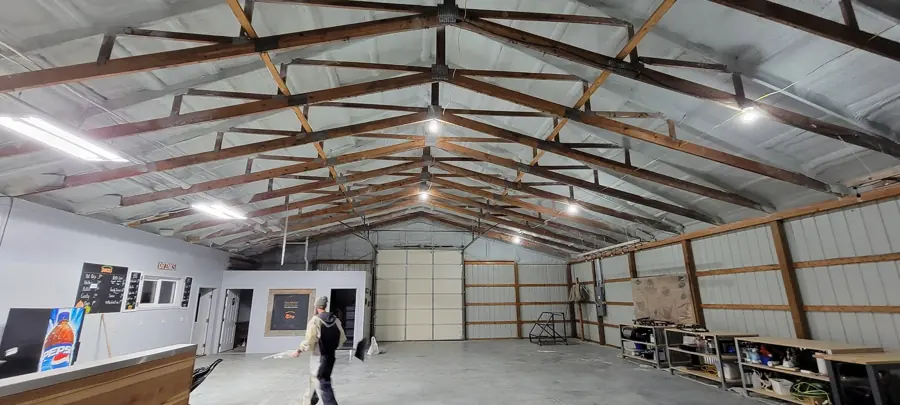 Large pole-barn style building with spray foam on the underside of the metal roof, wood trusses and a finished shop area