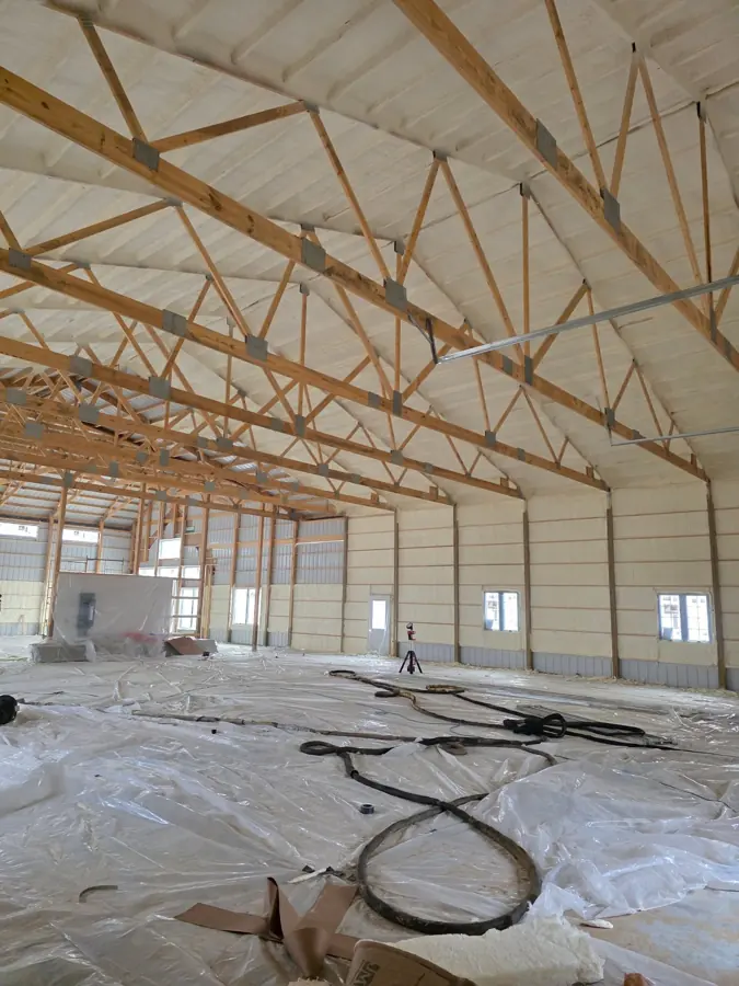 Large post-frame building with closed-cell spray foam on walls and roof deck, floor covered in plastic and hoses