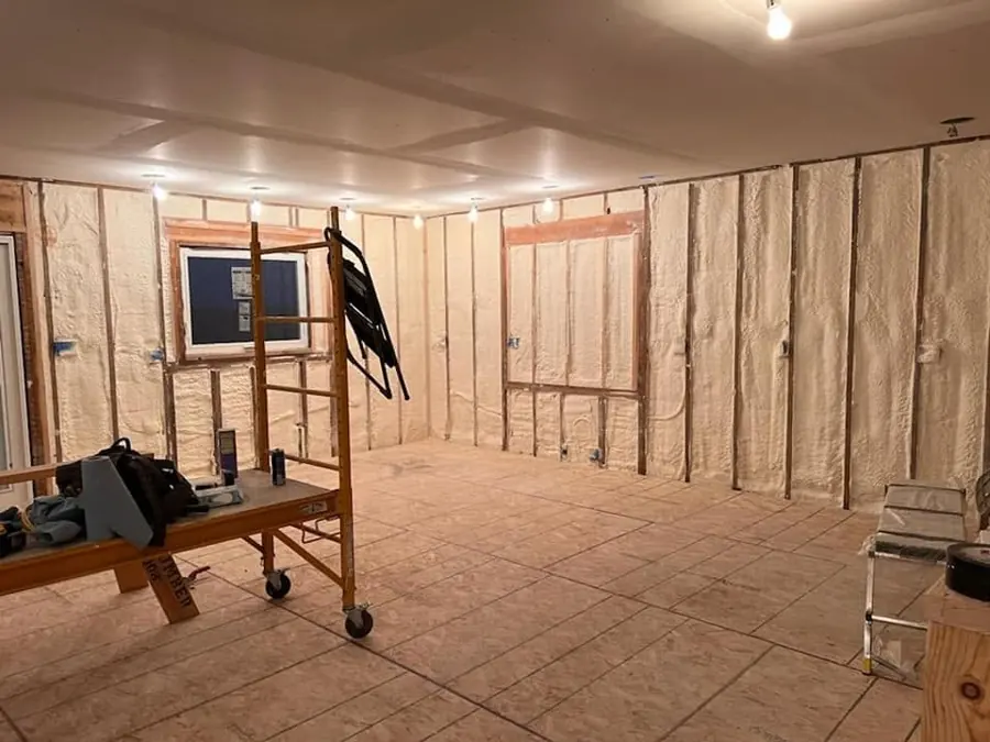 Room with spray foam insulation between wall studs, drywall already on the ceiling, scaffold and tools on an OSB floor