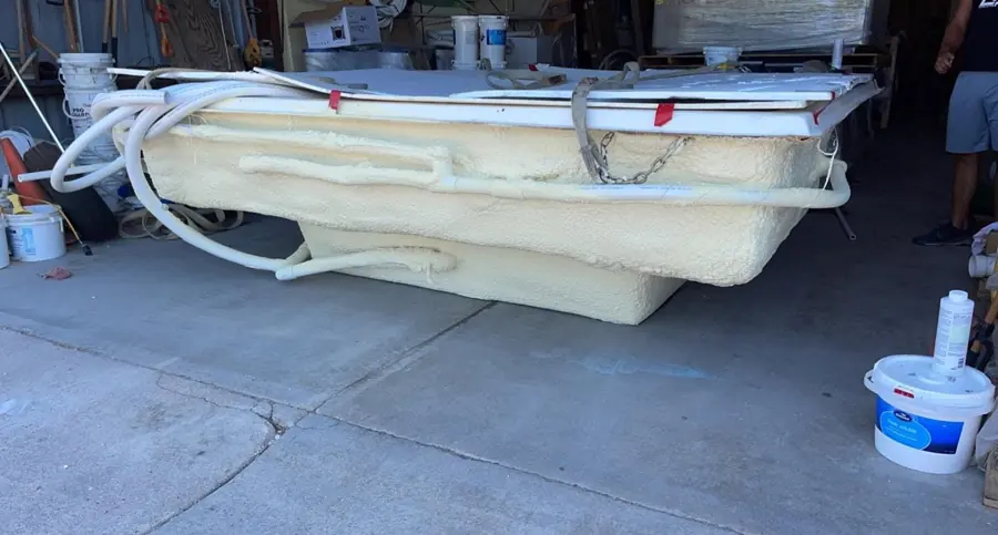 Side view of a tub shell coated in yellow closed-cell spray foam with foamed plumbing lines and a person standing nearby
