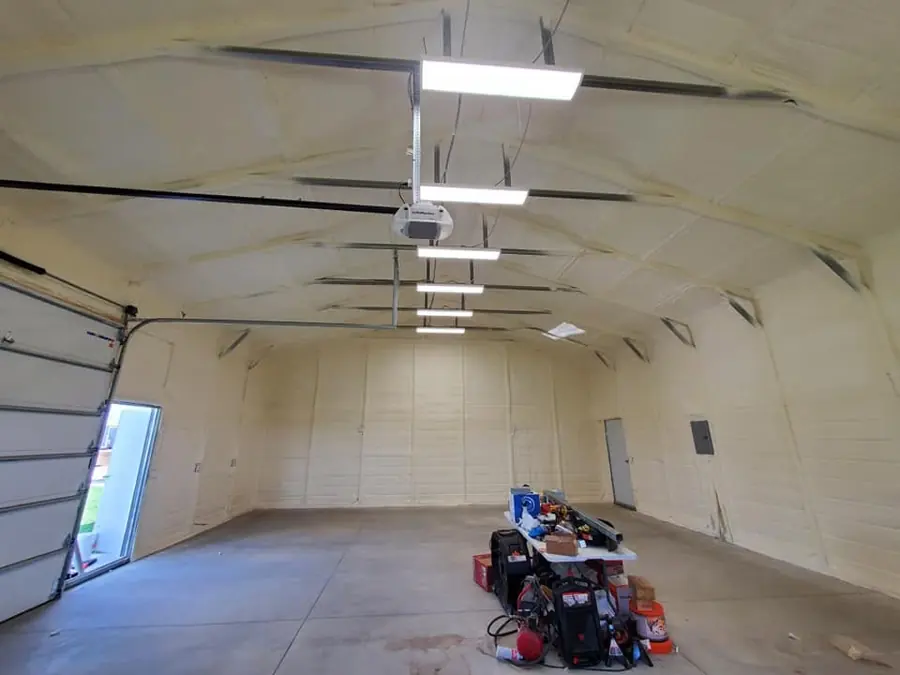 Garage with cream closed-cell spray foam on arched ceiling and walls, ceiling lights, door opener and an open side door