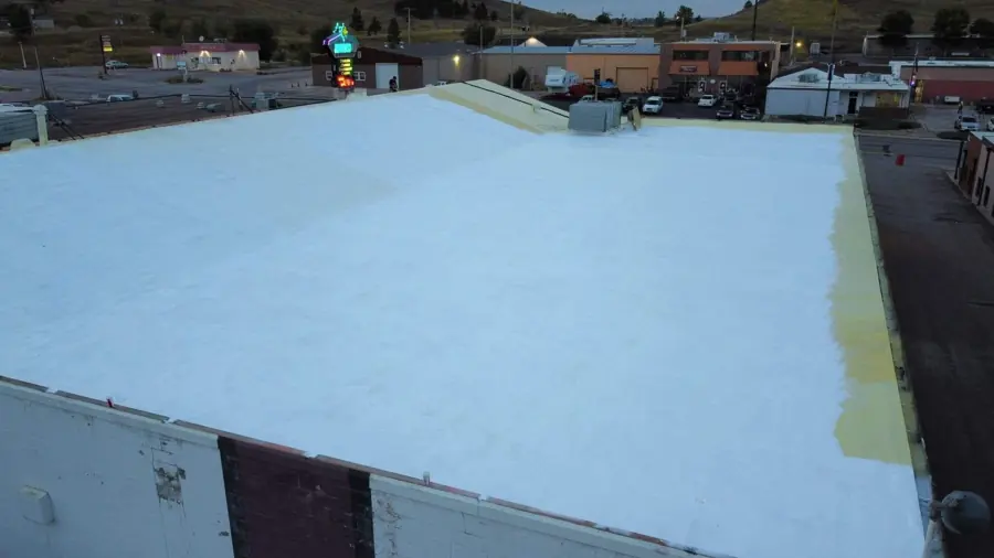 Drone view of a large commercial flat roof coated white with a strip of yellow foam still exposed at the edge