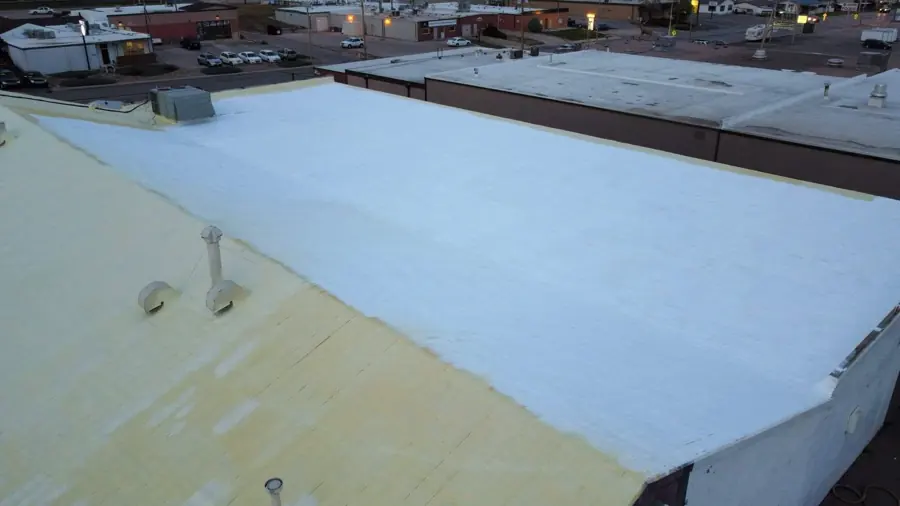 Drone view of a commercial roof with yellow spray foam on the left and white coating applied across the flat section