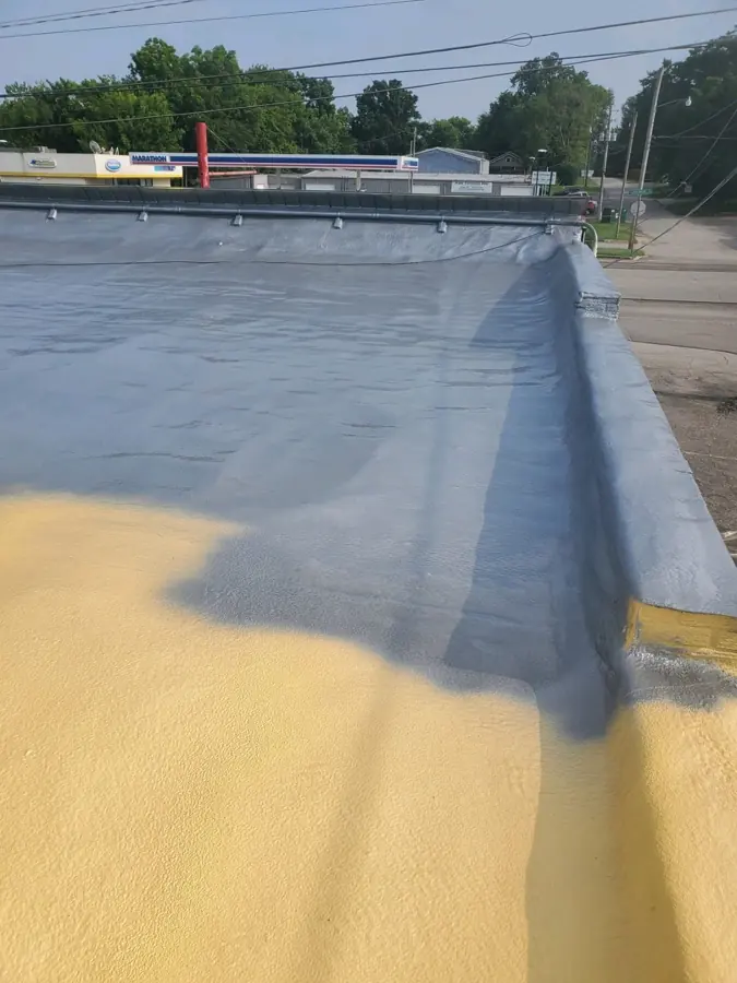 Flat roof with gray coating over the parapet and field, and yellow spray foam still bare in the foreground
