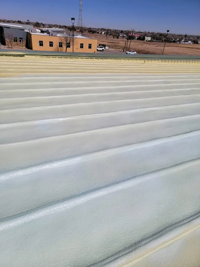 Ribbed metal roof coated in white over spray foam, with yellow foam still visible near the ridge