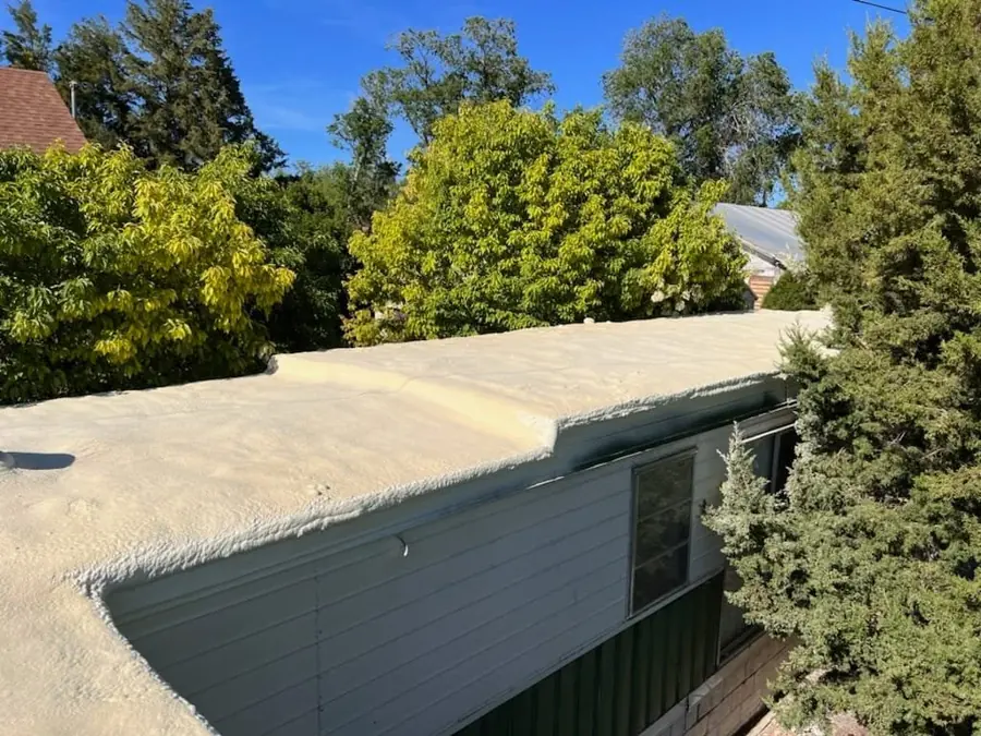 Uncoated tan spray foam covering a low-slope roof and wrapping the edge of a house with white siding